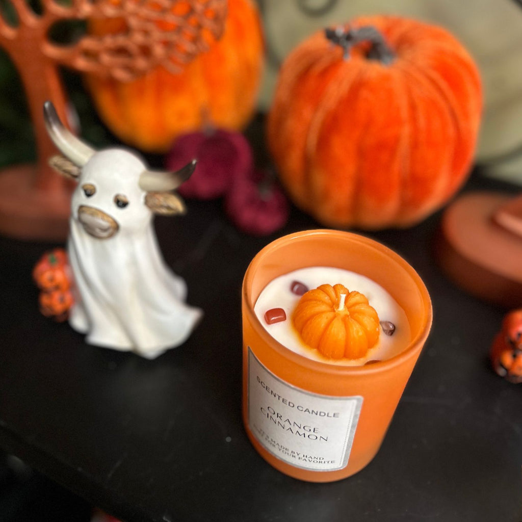 Candle with pumpkin design on a table with Halloween decorations