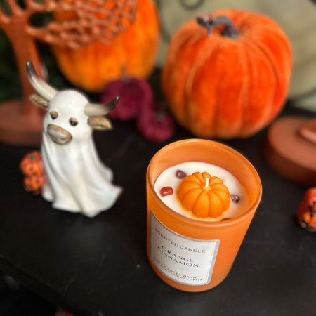 Candle with pumpkin design on a table with Halloween decorations