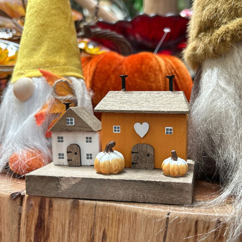 Decorative scene with gnomes, pumpkins, and small houses on a wooden surface.