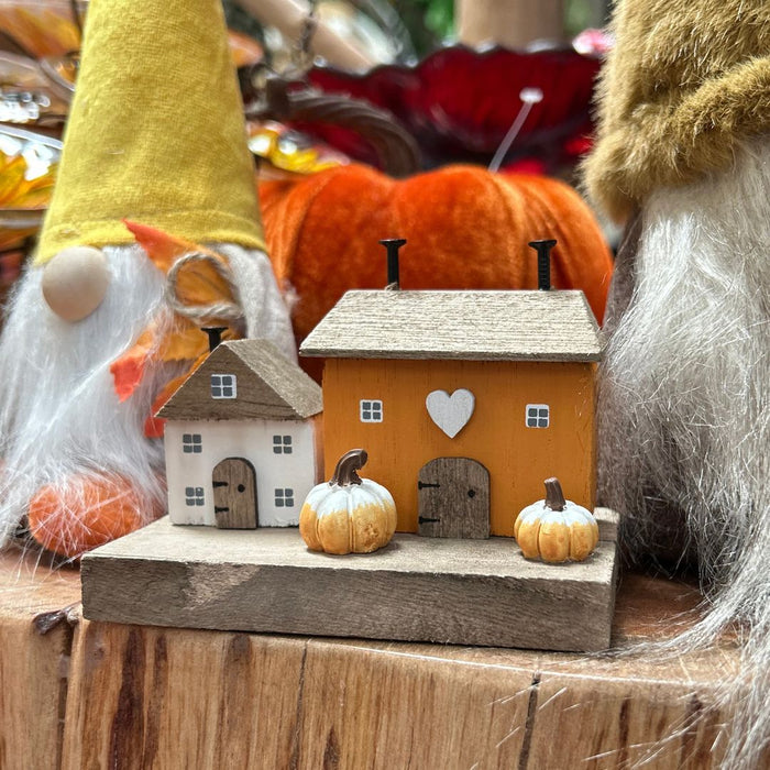 Decorative scene with gnomes, pumpkins, and small houses on a wooden surface.