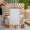 Decorative photo frame with wooden design held by a hand on a textured surface.