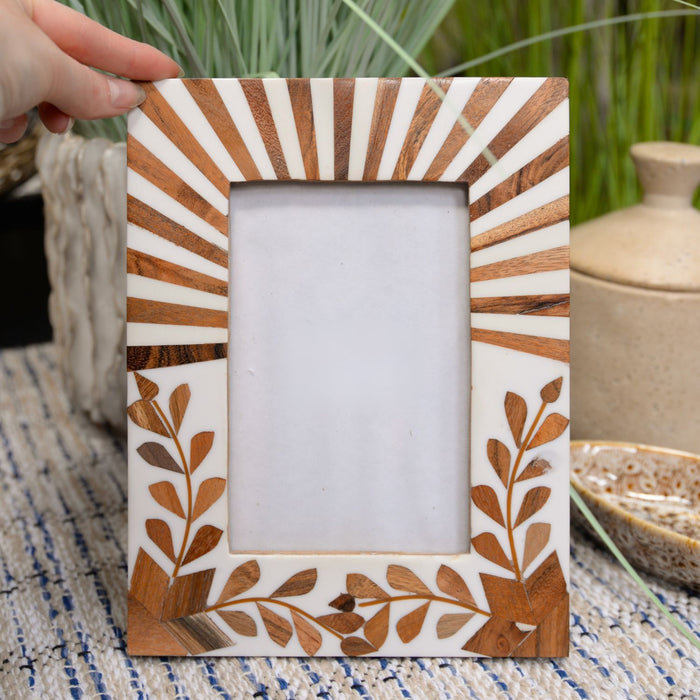 Decorative photo frame with wooden design held by a hand on a textured surface.