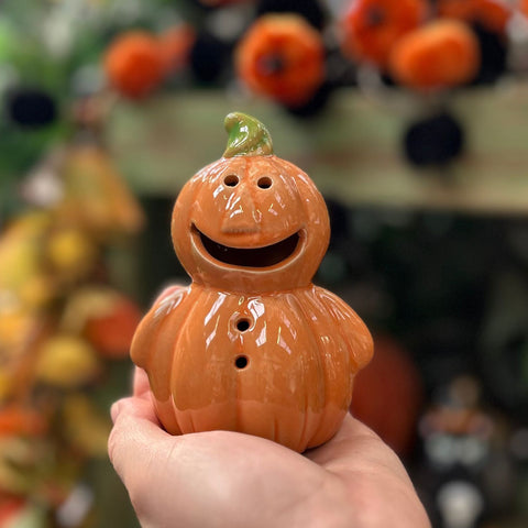 Ceramic pumpkin-shaped lantern held in a hand with blurred pumpkins in the background