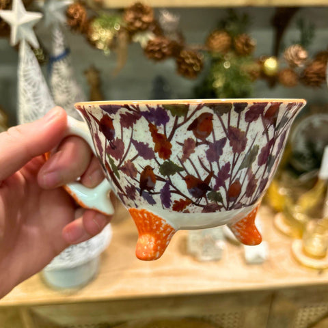 Hand holding a decorative cup with floral and bird pattern in a festive setting.