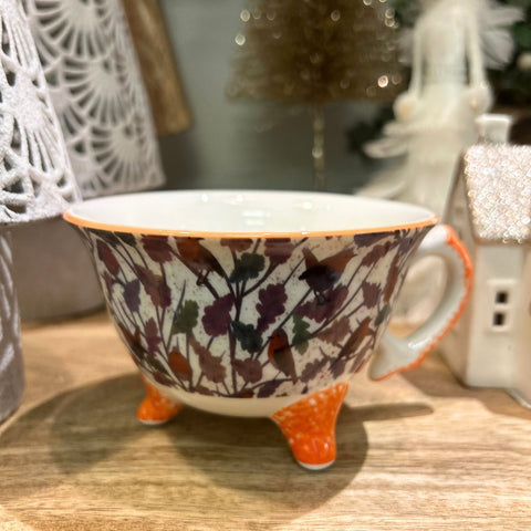 Decorative cup with floral pattern and orange accents on a wooden surface