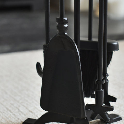 Set of black fireplace tools including a poker, tongs, and brush on a blurred background.