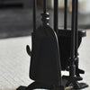 Set of black fireplace tools including a poker, tongs, and brush on a blurred background.