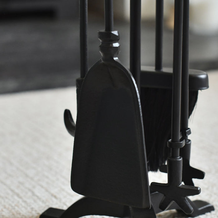 Set of black fireplace tools including a poker, tongs, and brush on a blurred background.