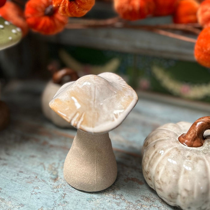 Decorative ceramic mushroom and pumpkin on a textured surface with blurred autumn decorations in the background.