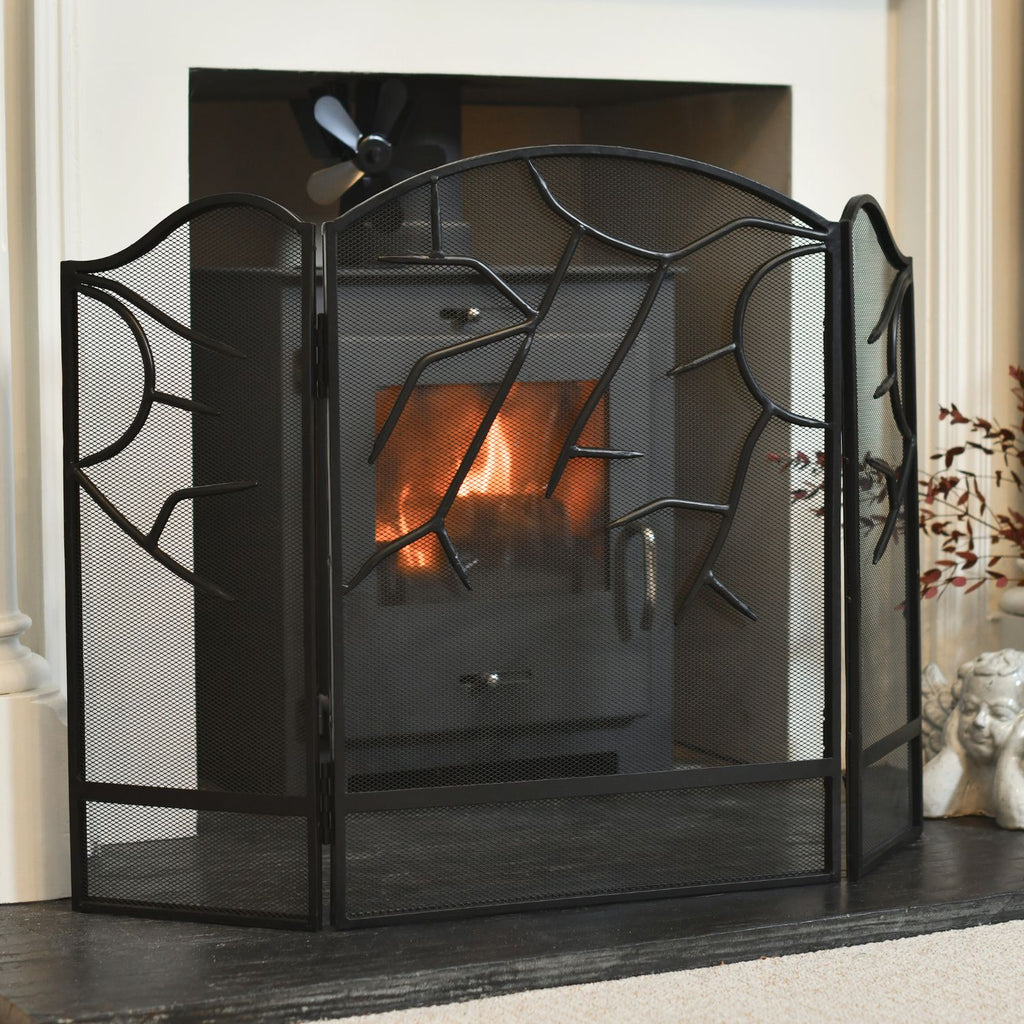 Black fireplace screen with decorative design in front of a lit fireplace.