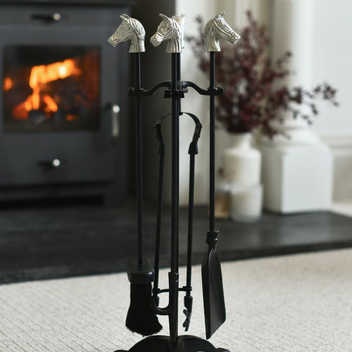 Set of fireplace tools with horse heads on a stand in front of a lit fireplace.