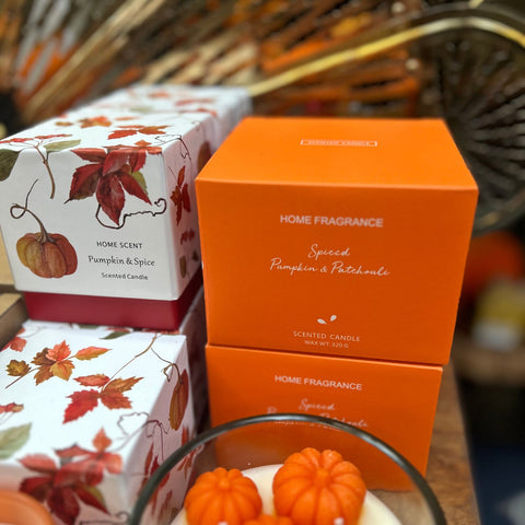 Home fragrance candles with autumn-themed packaging on a wooden surface.