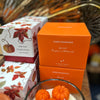Home fragrance candles with autumn-themed packaging on a wooden surface.