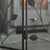 Black metal fireplace screen with leaf design in front of a fire.