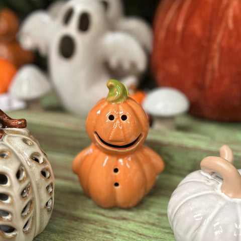Ceramic pumpkin with a face on a green surface with Halloween-themed decorations.