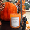 Orange cinnamon scented candle with a pumpkin and decorative elements in the background