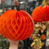 Orange honeycomb pumpkin decoration held by a hand with blurred Halloween decorations in the background.