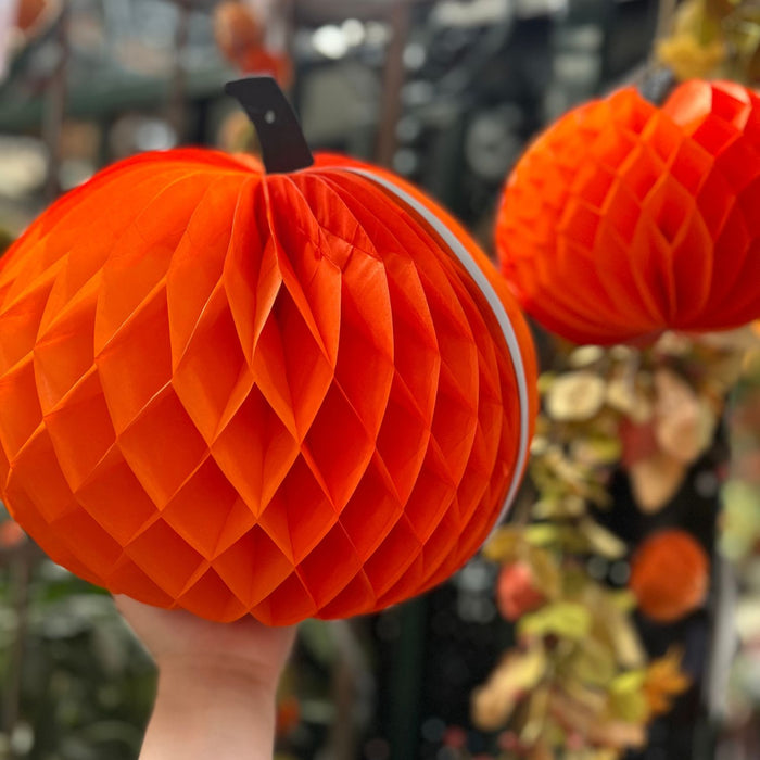 Orange honeycomb pumpkin decoration held by a hand with blurred Halloween decorations in the background.