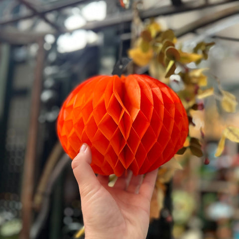 Hand holding a red honeycomb pumpkin decoration in a greenhouse setting