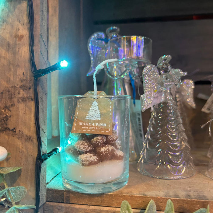 Decorative glass jar with a candle and angel figurine on a wooden surface with string lights.