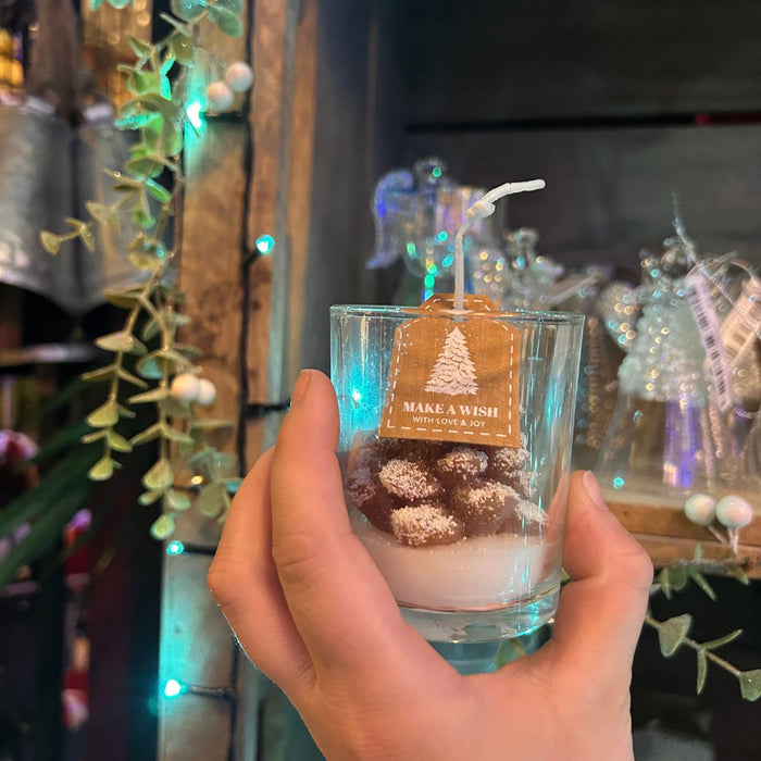 Hand holding a small glass with a candle and decorative tag against a festive background.