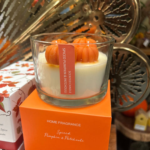 Candle with pumpkin design on an orange box labeled 'Home Fragrance' in a decorative setting.