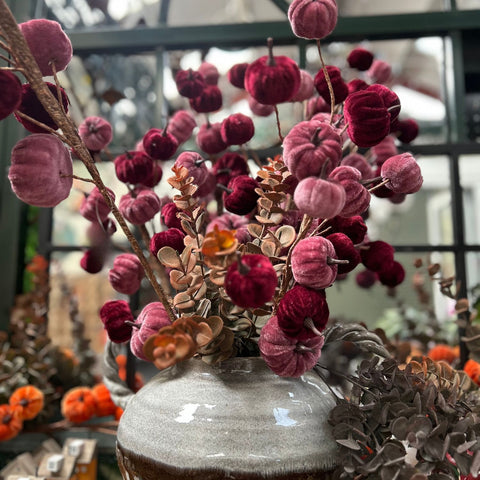 Decorative arrangement of pink and red berries in a clear vase with a blurred indoor background.
