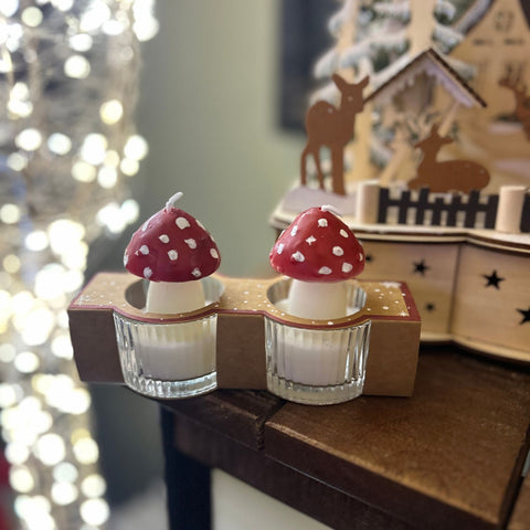 Two small candles with mushroom design on a decorative stand in front of a blurred festive background.