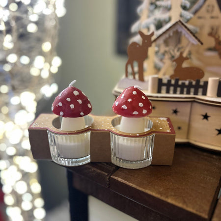 Two small candles with mushroom design on a decorative stand in front of a blurred festive background.