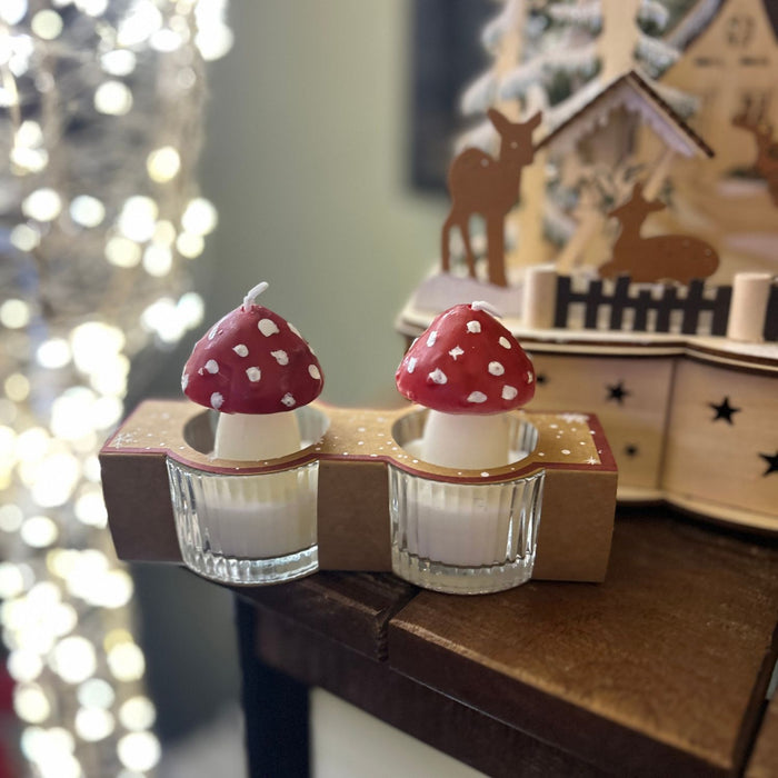 Two small candles with mushroom design on a decorative stand in front of a blurred festive background.