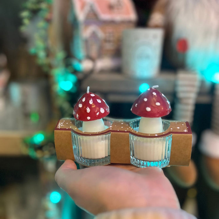 Two small mushroom-shaped candles in a holder with a blurred background