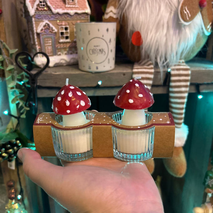 Two small candles with red mushroom tops held in a hand against a festive background.
