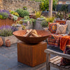 A large weathered metal fire pit bowl filled with logs,