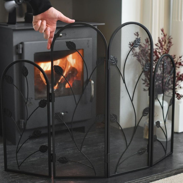 Person adjusting a decorative fireplace screen in front of a burning fireplace.