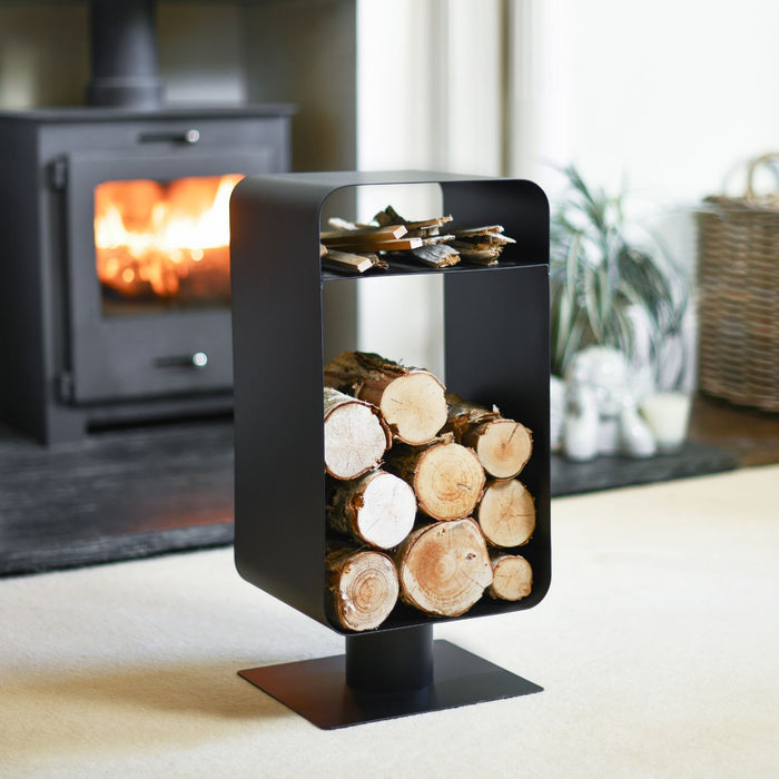 Black metal firewood holder with logs in front of a burning stove.