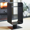 Black metal contemporary log store against a blurred indoor background with a fireplace.