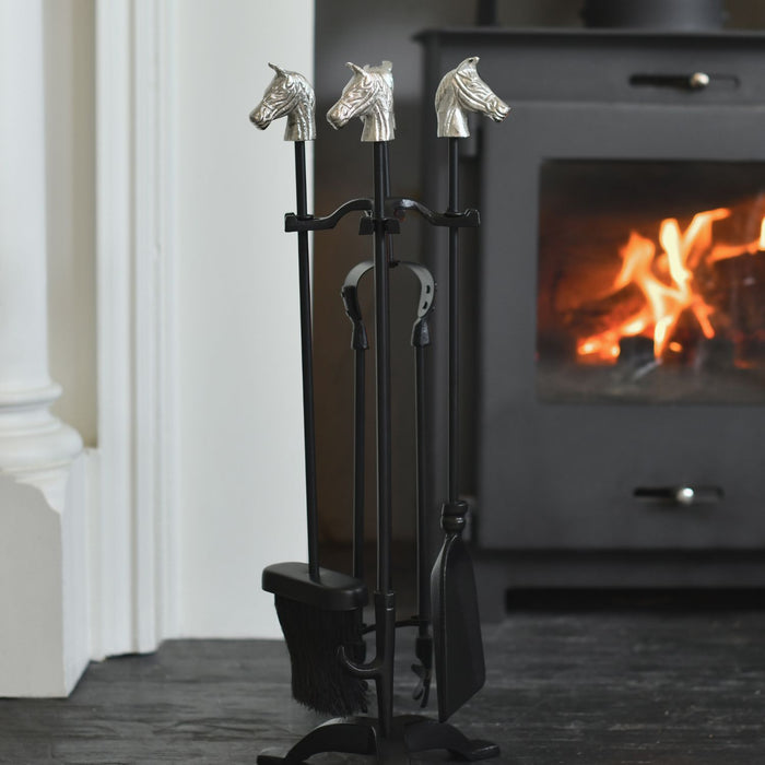 Set of fire tools with horse heads in front of a burning fireplace.