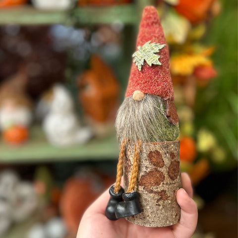 Hand holding a small gnome figurine with a red hat and brown body against a blurred background.