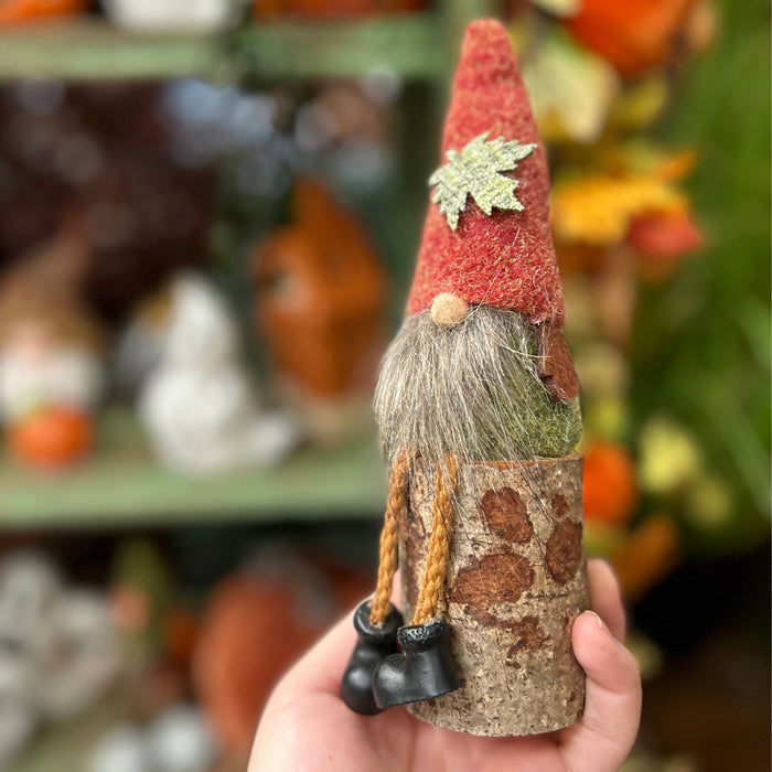 Hand holding a small gnome figurine with a red hat and brown body against a blurred background.