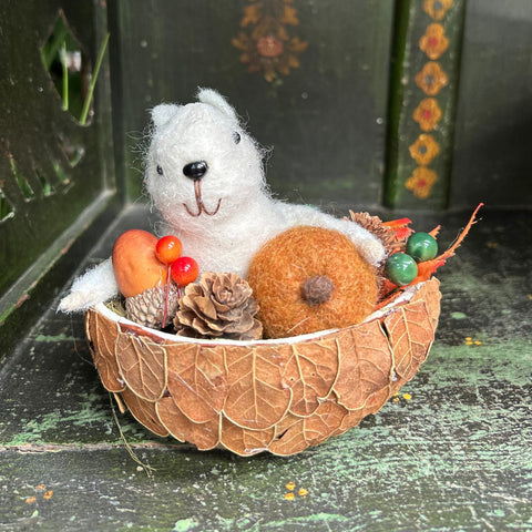 White felt mouse in a leaf bowl with autumn decorations on a textured surface