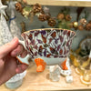 Hand holding a decorative cup with floral patterns and orange feet against a festive background.