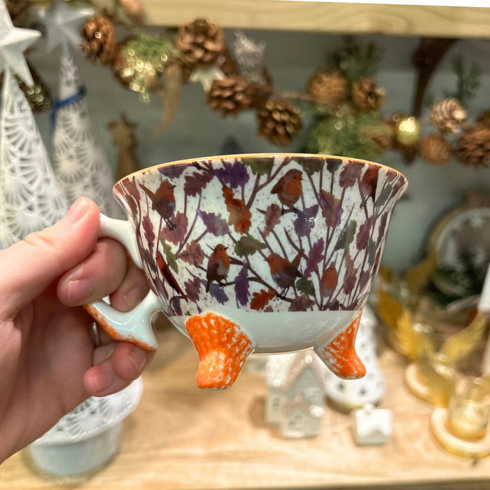 Hand holding a decorative cup with floral patterns and orange feet against a festive background.