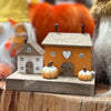 Decorative miniature houses with pumpkins on a wooden base, autumn-themed setting.